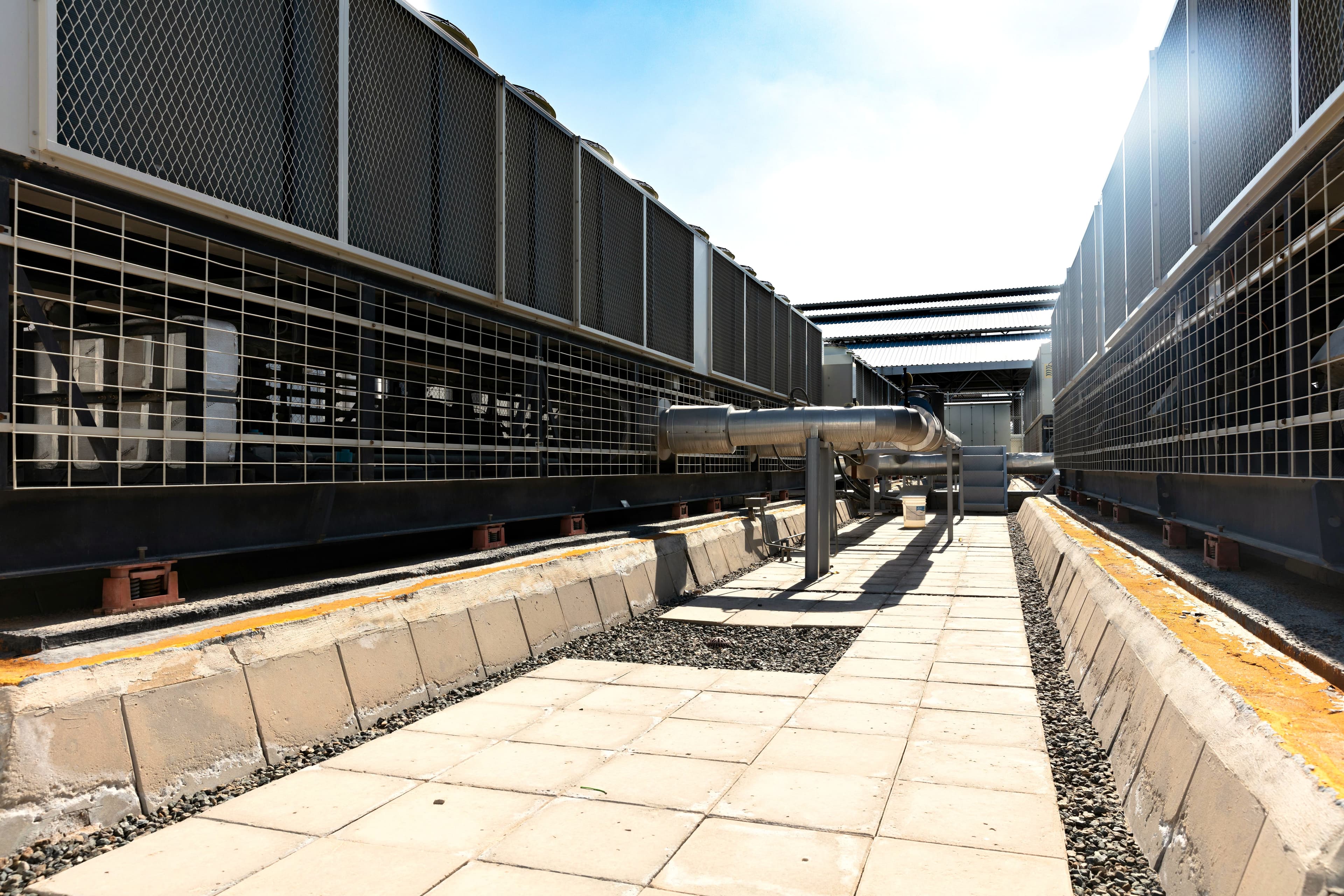 Rows of air-cooled chiller units flanking a rooftop walkway